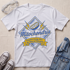 A white short-sleeve graphic T-shirt laid flat on a light fabric background, styled with clear safety goggles, gray sneakers, and a blue denim jacket. The shirt has a large front graphic reading “Mitochondria” with a football motif and the phrase “Premium Energy Since the Dawn of Eukaryotes.