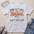 A white graphic t-shirt laid flat on a beige textured background, styled with safety goggles, sneakers, and a denim jacket. The t-shirt features a humorous physics joke printed in orange, teal, and dark gray text.