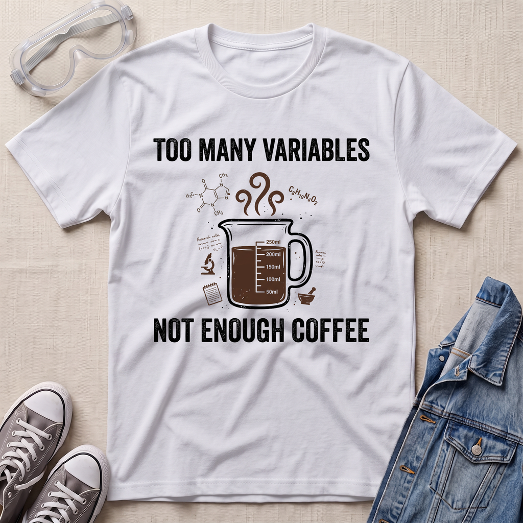 A white graphic t-shirt laid flat on a light beige textured background, styled with clear safety glasses, gray sneakers, and a blue denim jacket. The t-shirt features a dark brown coffee mug graphic with steam and the text 'TOO MANY VARIABLES NOT ENOUGH COFFEE' in black.